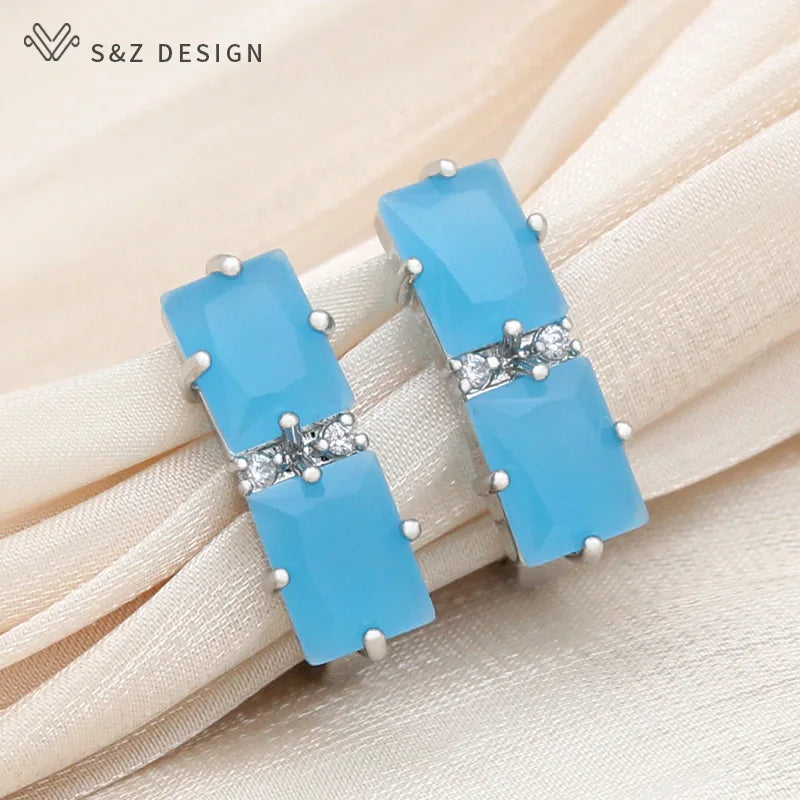 Brincos pendentes de cristal azul-azulado vivo com montagem em tom de prata e ponte de strass sobre tecido beige plissado