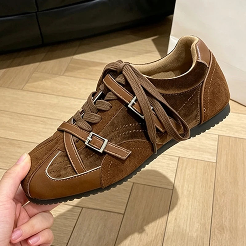 Side profile of brown suede sneaker held in hand showing silver buckle straps and white stitching
