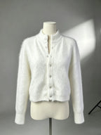 Cardigan longo branco felpudo em manequim contra fundo cinzento, destacando tecido texturizado, gola levantada e silhueta ajustada