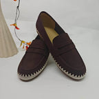 Mocassini slip-on marrone scuro con punta tonda e cuciture bianche seghettate accanto a foglie arancioni
