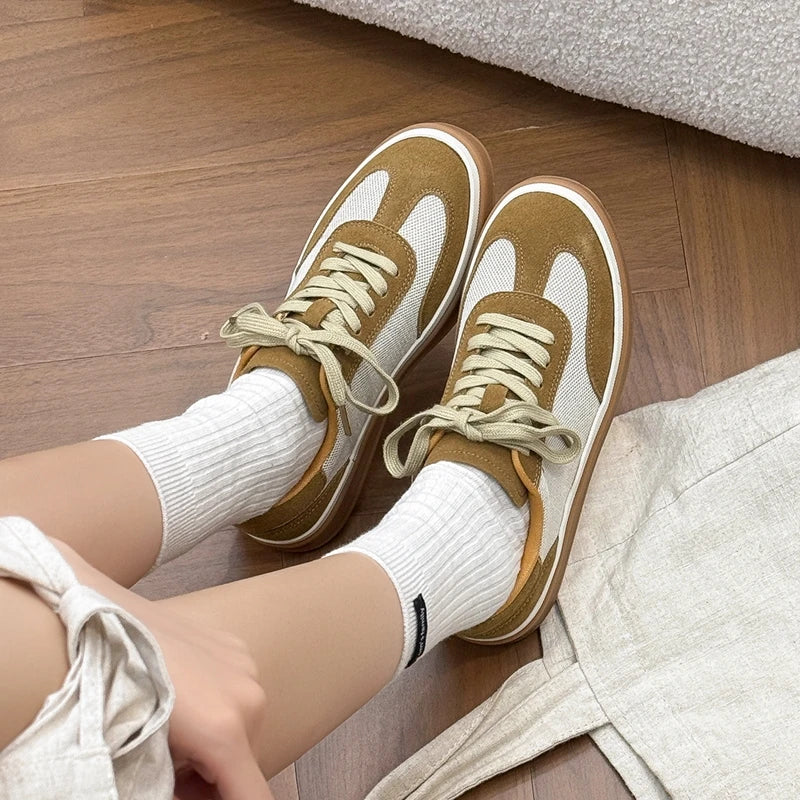 Top-down view of feet on wood floor next to linen, showing white mesh toe box and caramel suede overlays
