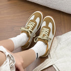 Top-down view of feet on wood floor next to linen, showing white mesh toe box and caramel suede overlays