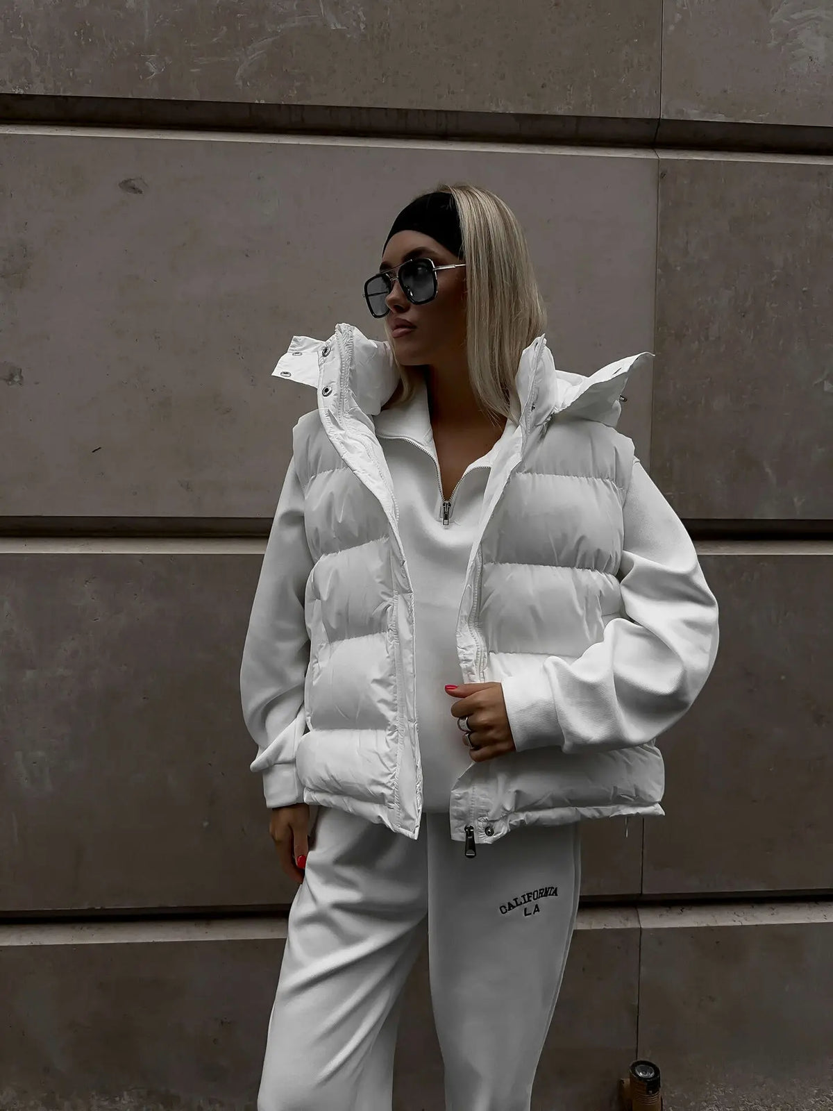 Close-up do colete branco com capuz aberto, revelando detalhe do zíper e design de gola alta