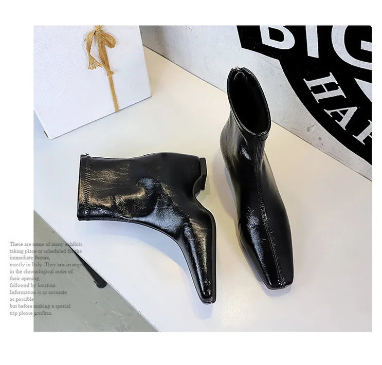 Foto artística de botas pretas texturizadas deitadas e em pé junto a uma caixa de presente