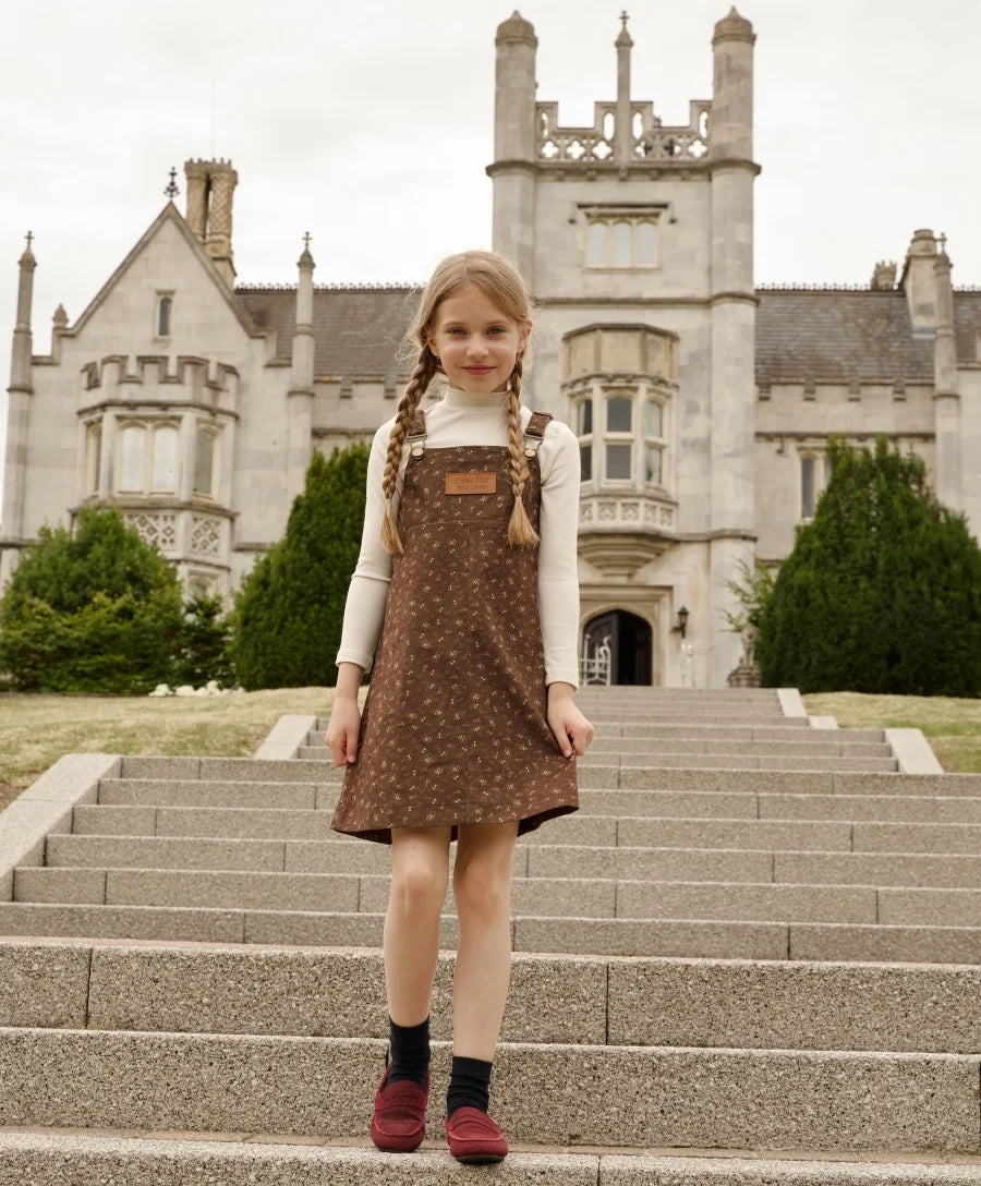 Menina com vestido de alças floral e gola alta creme nas escadas de um castelo