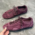 Hand holding deep burgundy sneaker to show rounded toe and dark laces with white accents