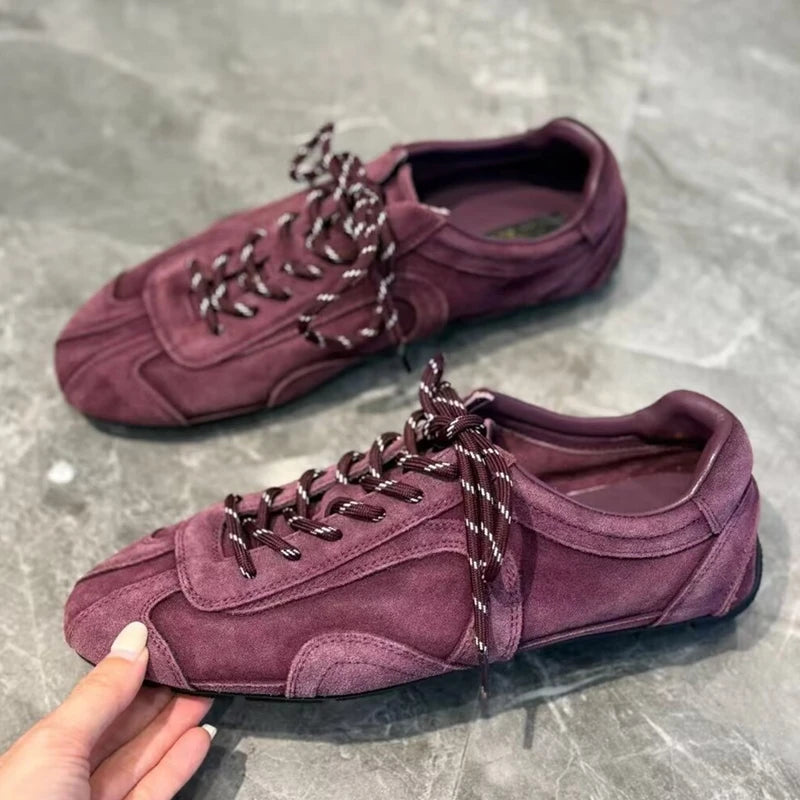 Hand holding deep burgundy sneaker to show rounded toe and dark laces with white accents