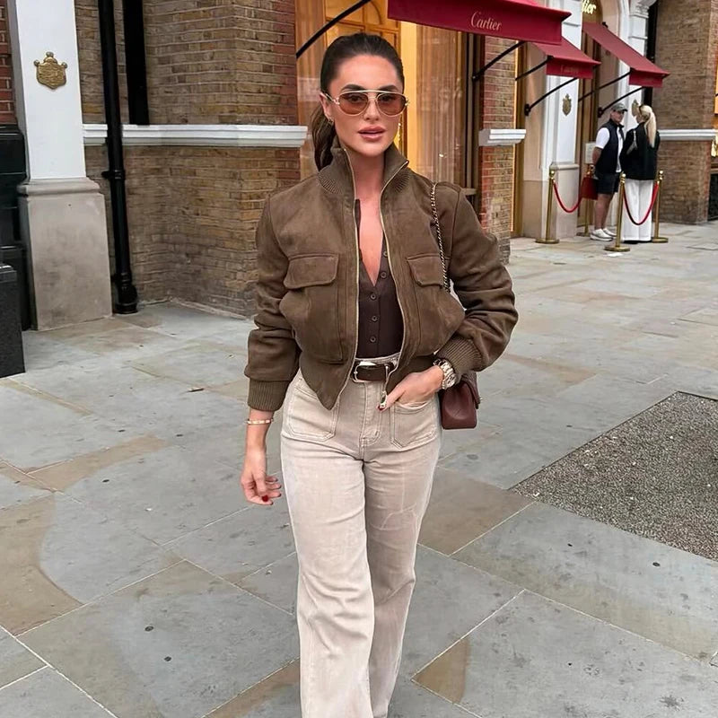 Jaqueta bomber estilo suede castanha com acabamento canelado, jeans flare e óculos aviador em ambiente urbano.