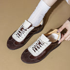 Toma cenital de zapatillas marrones sujetadas por mano mostrando laterales de cuero oscuro, puntera de ante y protectores de cordón blancos