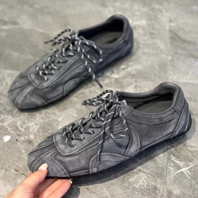 Hand holding grey suede sneaker demonstrating flexibility and side panel stitching