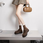 Ganzkörperaufnahme des Modells in braunen Punkt-Mules, gestylt mit Houndstooth-Rock und beiger Handtasche auf silbernem Metallbänkchen