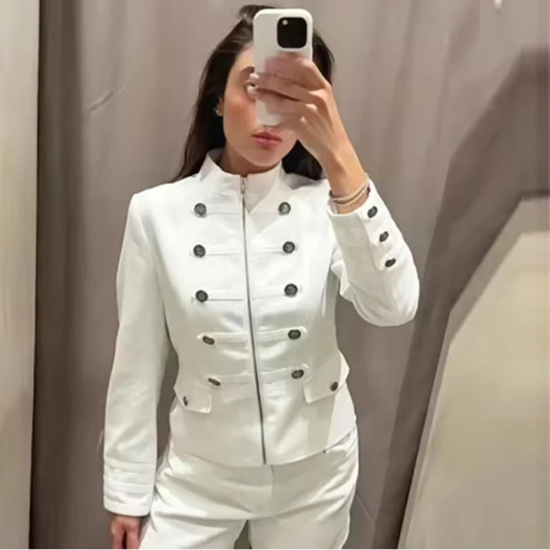 Modelo usa jaqueta militar branca ajustada com botões escuros e calças combinantes, tirando selfie no espelho do provador