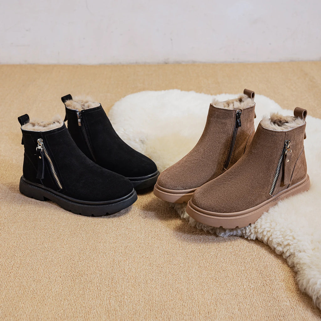 Botas de nieve negras y marrones de ante vacuno con forro de felpa y cremalleras laterales sobre alfombra beige junto a un accesorio de piel de oveja