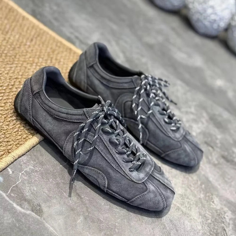 Charcoal grey suede sneakers on marble floor emphasizing matte finish and minimalist design