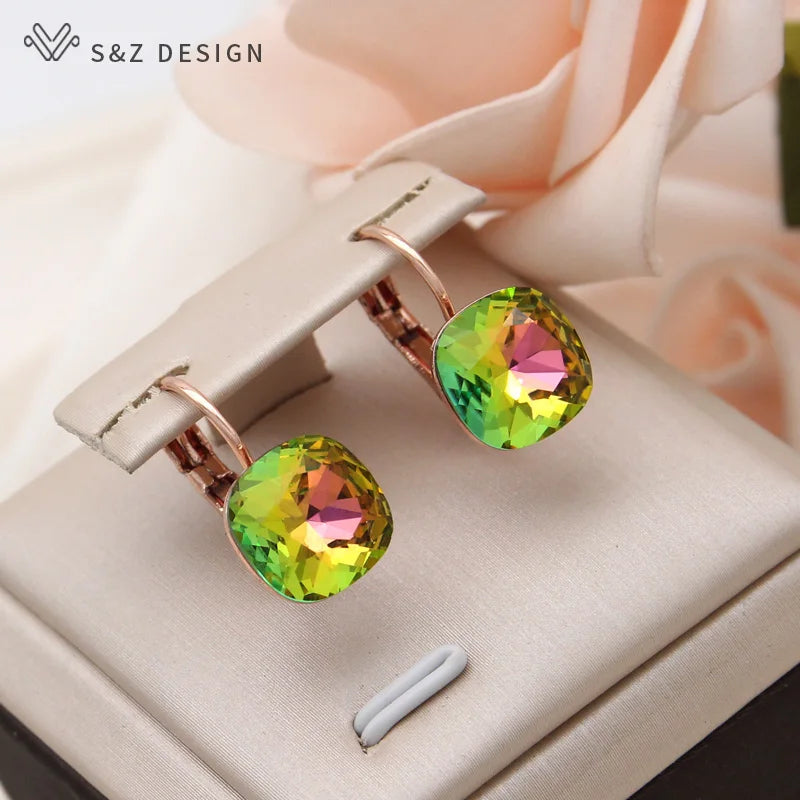 Brincos gota quadrados com gemas iridescentes verde e amarelo em ganchos de pressão dourado-rosé sobre display bege