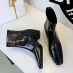 Botas pretas brilhantes de bico quadrado com painel elástico ao lado de uma caixa de presente na mesa