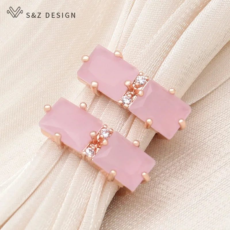 Brincos de cristal retangulares cor-de-rosa suave com presilhas em tom de rosa e strass central sobre tecido creme