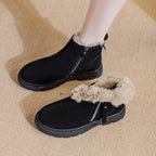Modelo usando botines de ante negros, uno abrochado y otro desabrochado con puño de pelo hacia abajo sobre alfombra beige