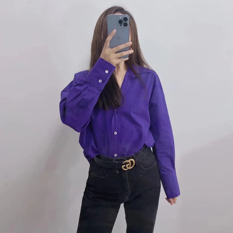 Modella indossa camicia bottoni viola scuro dentro jeans neri con cintura logo oro