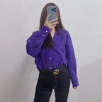 Modella indossa camicia bottoni viola scuro dentro jeans neri con cintura logo oro