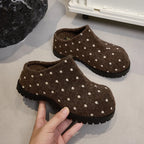 Nahaufnahme dunkelbrauner Punkt-Filzclogs mit dicken schwarzen Stegen, gehalten an einem Steinprop zur Hervorhebung des flauschigen Materials