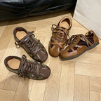 Four scattered retro sneakers in brown and olive tones near a black leather sofa and shopping bag