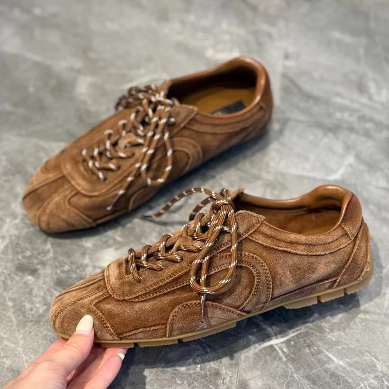 Hand holding warm brown sneaker revealing grooved tread pattern and stitched overlays