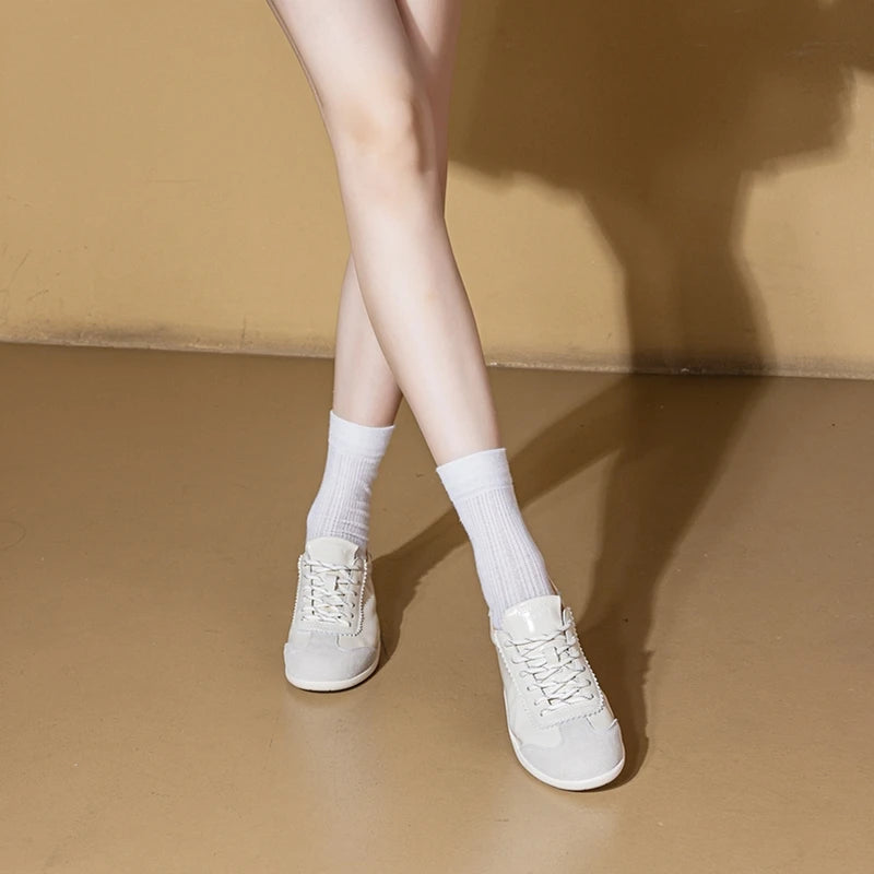 Piernas cruzadas de modelo usando zapatillas lace-up blancas y calcetines altos sobre suelo tan contra pared beige