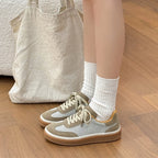 Woman standing in beige and white patchwork sneakers with gum sole and white socks next to tote bag