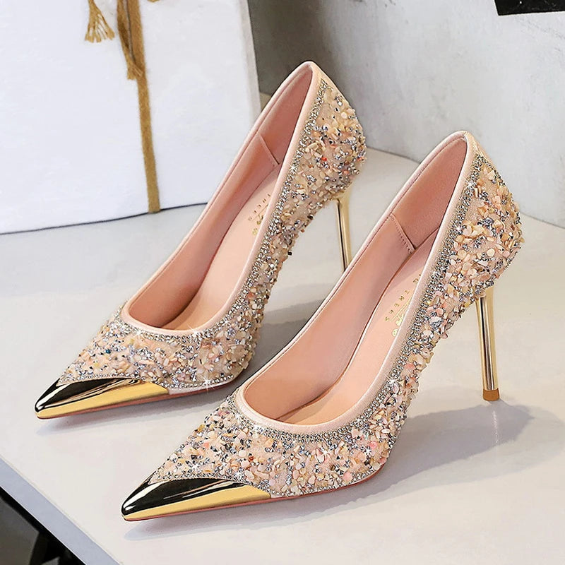 Champagnerfarbene Pumps mit Goldmetall-Zehenkappe und Stiletto-Absatz auf weißer Oberfläche