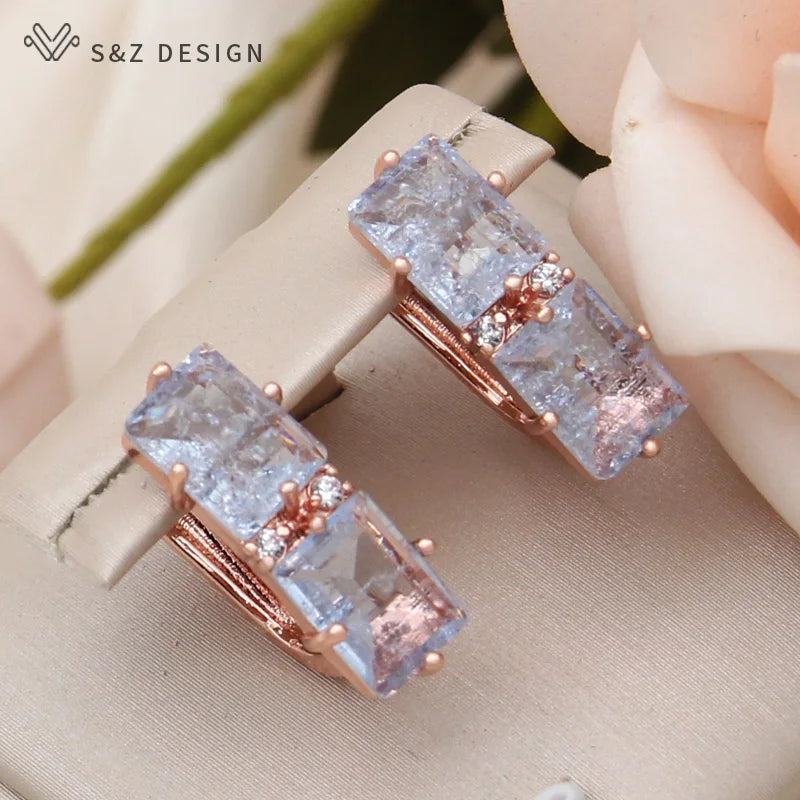Close-up de brincos geométricos em ouro rosa com pedras azuis claras texturizadas e zircônia cúbica
