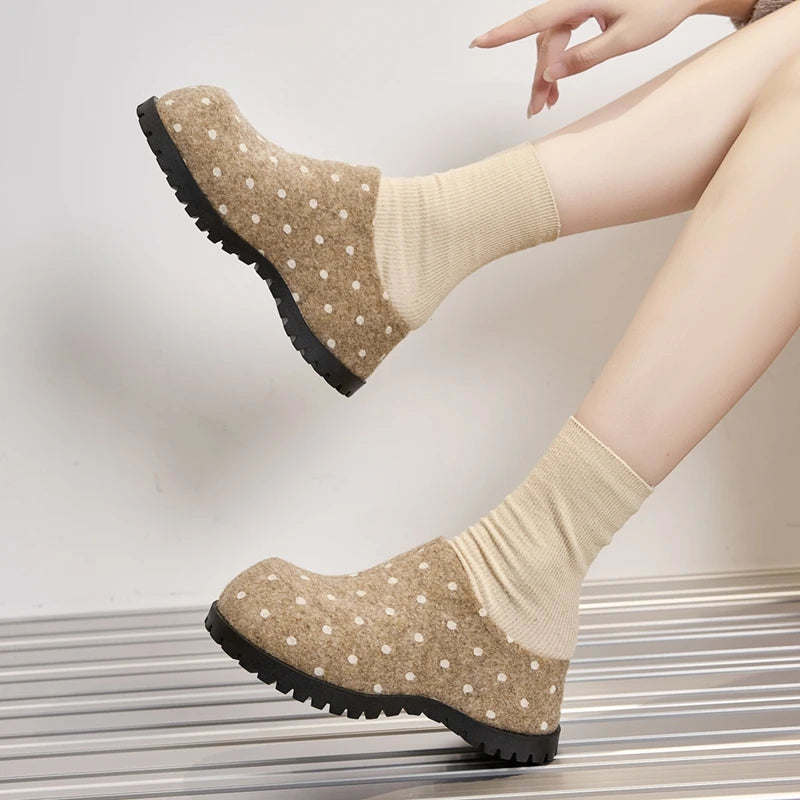 Gekreuzte Beine des Modells in beige Punkt-Mules und cremefarbenen Socken, die die Seitenansicht und den klobigen schwarzen Absatz hervorheben