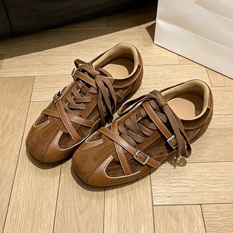 Brown mixed-material sneakers with round toe, cross-straps, and silver buckles on light wood floor