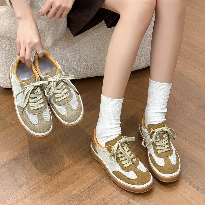 Model holding brown patchwork sneakers while wearing them with white socks on wooden floor