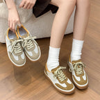 Model holding brown patchwork sneakers while wearing them with white socks on wooden floor