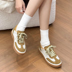 Side profile of crossed legs in sneakers, showing medium heel, tan suede patches, and lace-up closure
