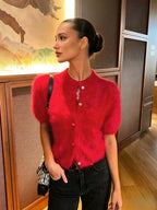 Perfil lateral de modelo com cardigan curto felpudo vermelho vibrante com gola redonda e botões claros, combinado com jeans pretos