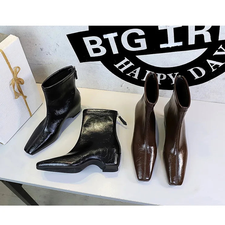 Quatro botas de bico quadrado em preto e marrom dispostas sobre superfície branca perto de um letreiro