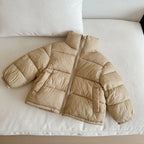 Beige light tan padded jacket on white sofa emphasizing smooth synthetic fabric texture and elasticized cuffs.