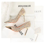 Beige Pailletten-Heels mit Goldspitzen, die neben Federn auf Markenboxen ruhen