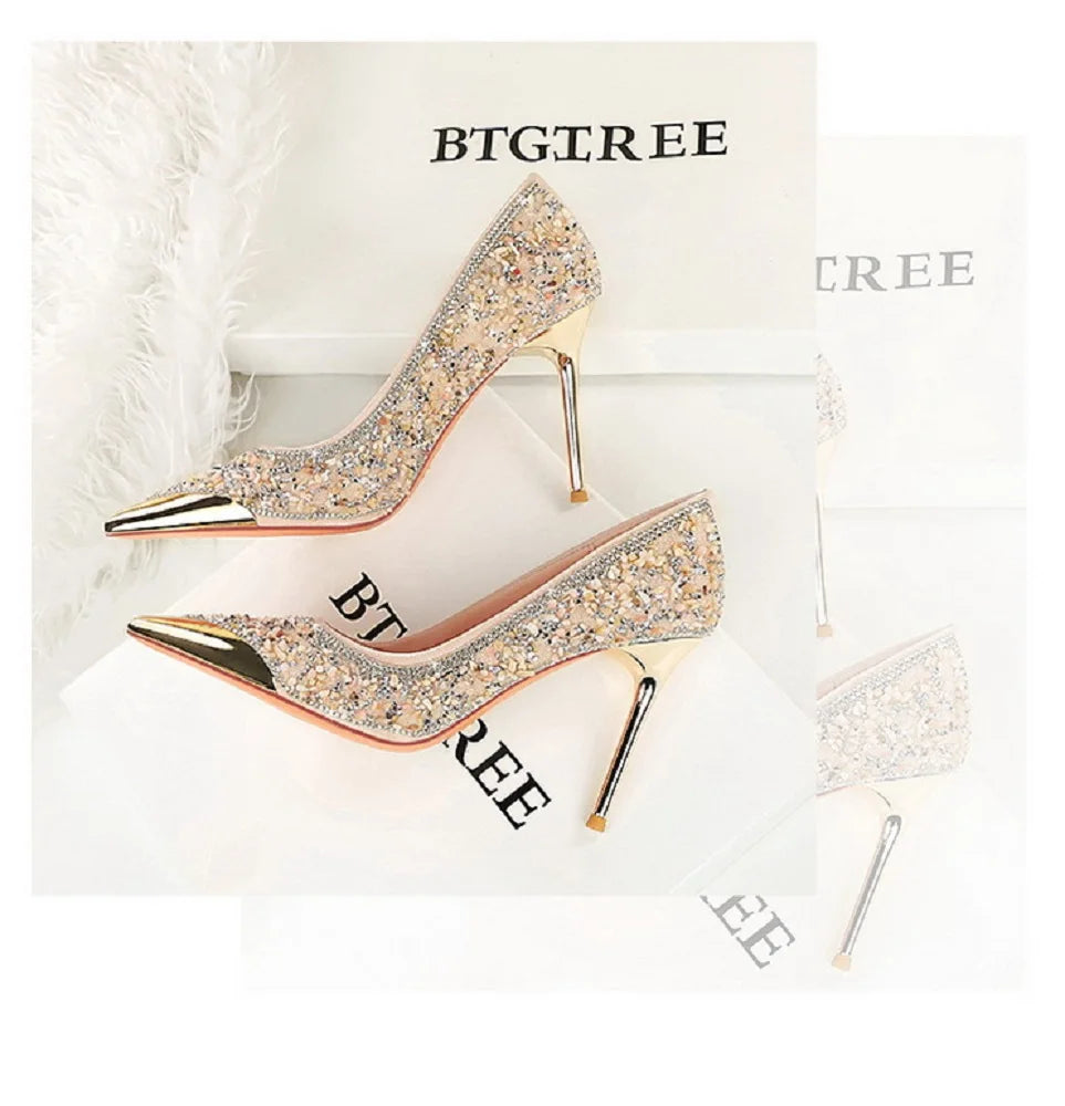 Beige Pailletten-Heels mit Goldspitzen, die neben Federn auf Markenboxen ruhen