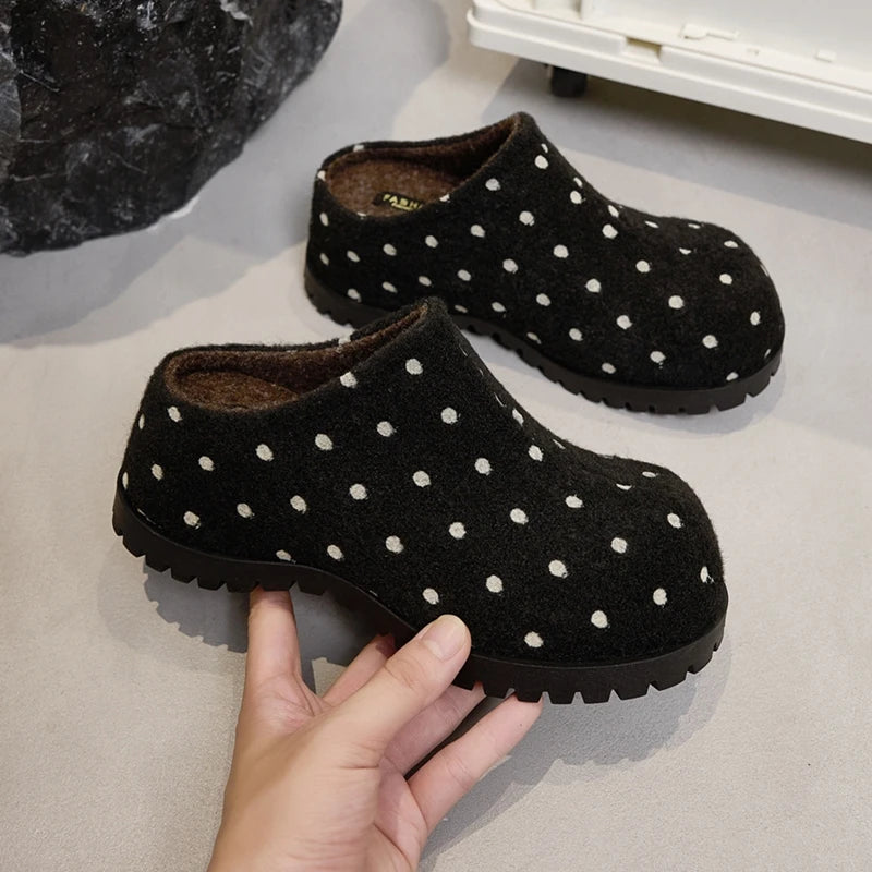 Schwarze Filz-Mule-Clogs mit hochkontrastierenden weißen Punkten und dicker Stegsohle, von der Hand gehalten zur Größenveranschaulichung