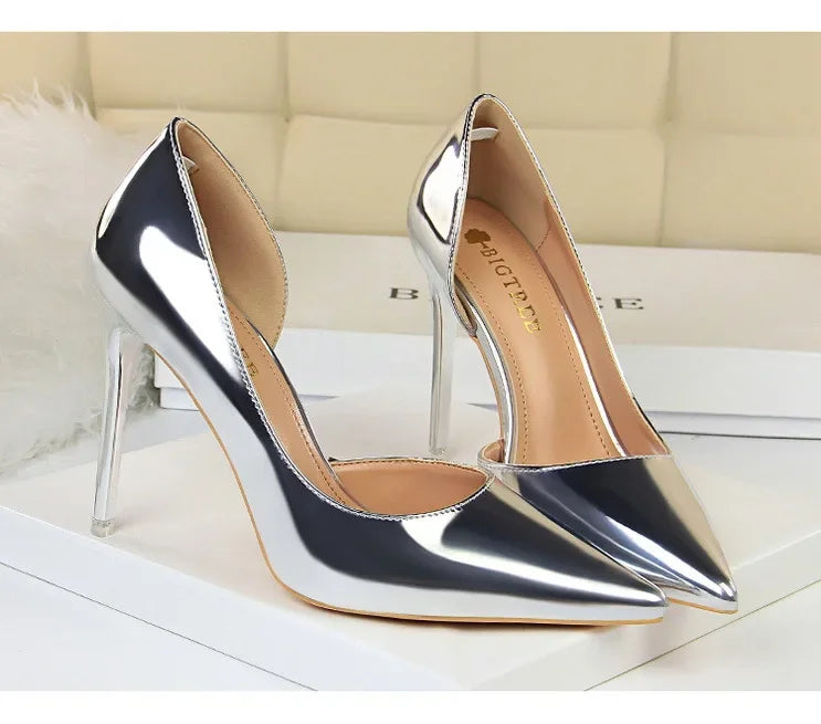 Metallische Silber-Pumps mit spitzem Zeh und transparentem Stilettoabsatz auf weißer Oberfläche, goldenes BIGTREE-Logo auf brauner Innensohle