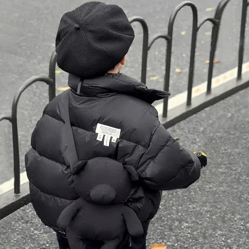 Back view of child in black heavyweight puffer jacket with white label patch and bear-shaped backpack.