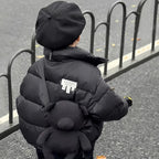 Back view of child in black heavyweight puffer jacket with white label patch and bear-shaped backpack.