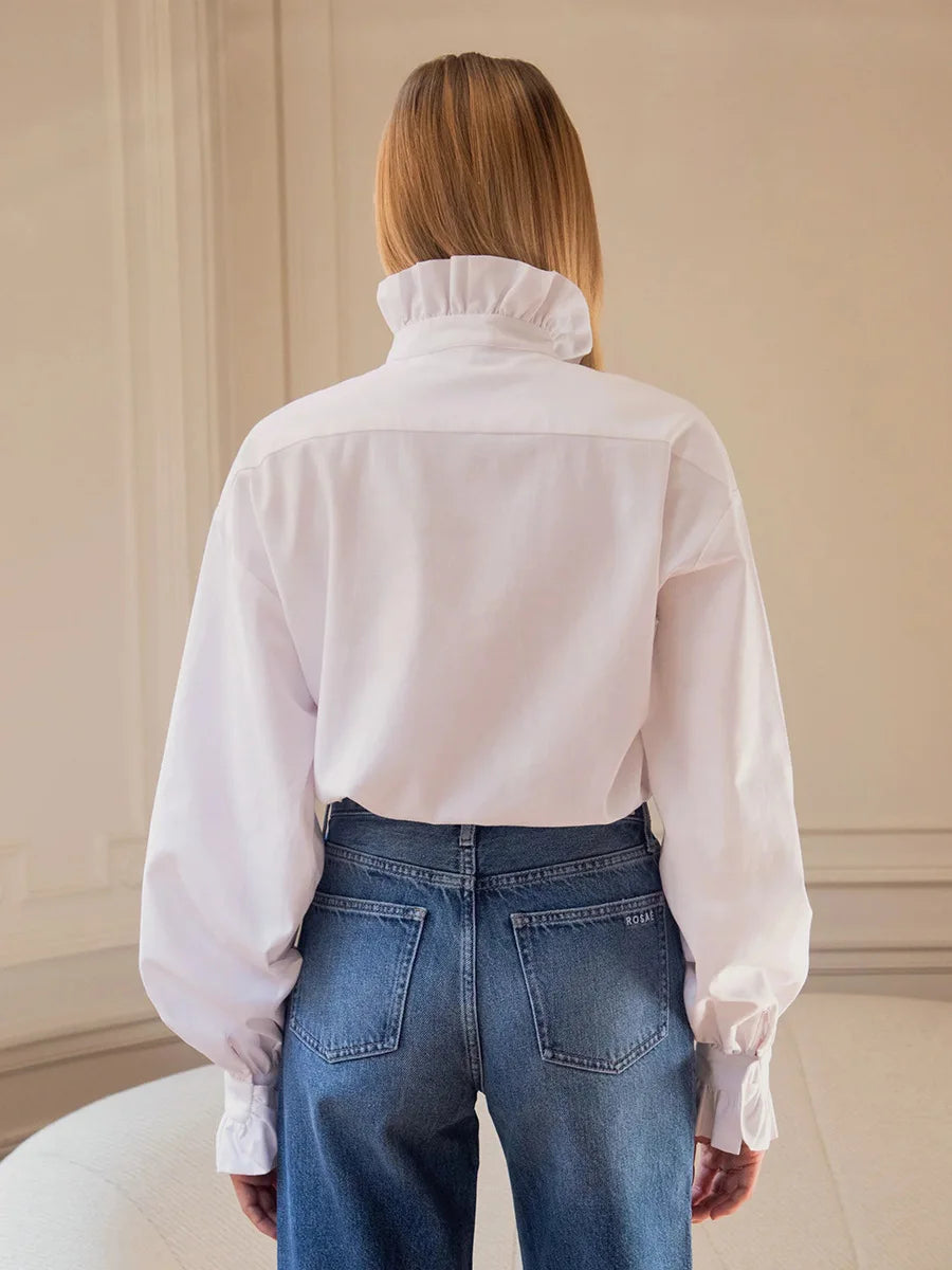 Rückansicht: Weißes Hemd mit sauberem Rückenpanel und hohem Rüschenkragen über blauen Jeans sichtbar