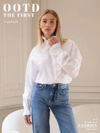 Modell im weißen Hemd mit Stehkragen und Rüschenverschluss, stilvoll mit Jeans vor beiger Wand mit Dekorationen