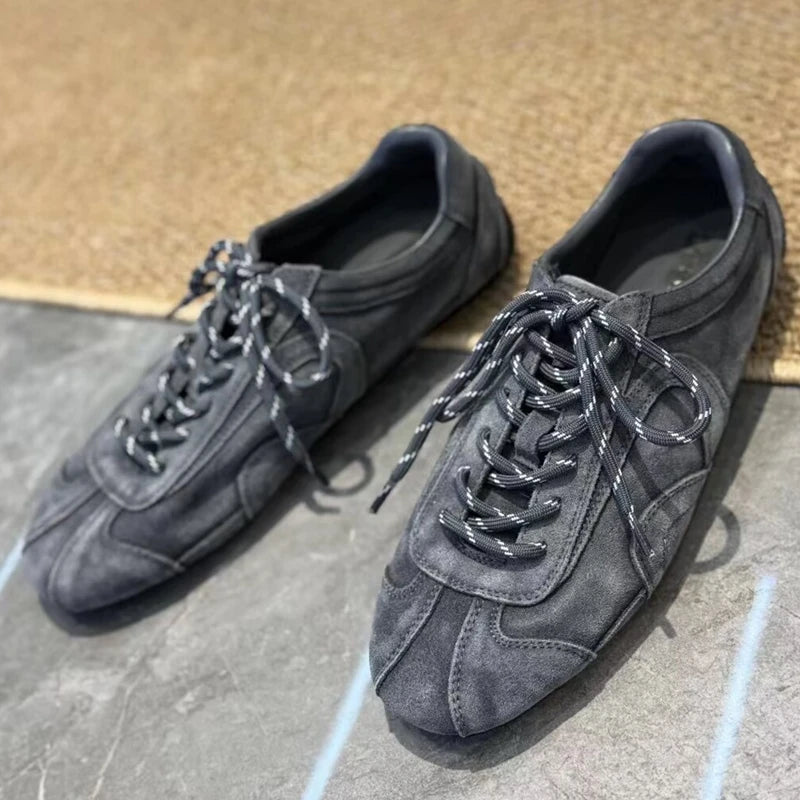 Front view of grey suede flats displaying symmetrical laces and low-profile rubber sole