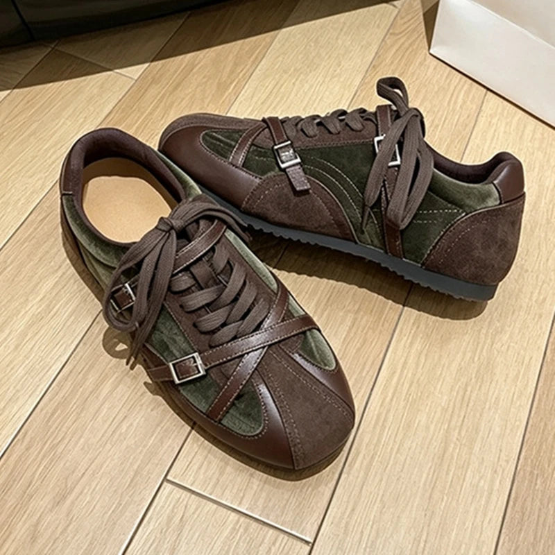 Two-tone olive green and brown retro sneakers with cross-strap buckles and dark laces on wood