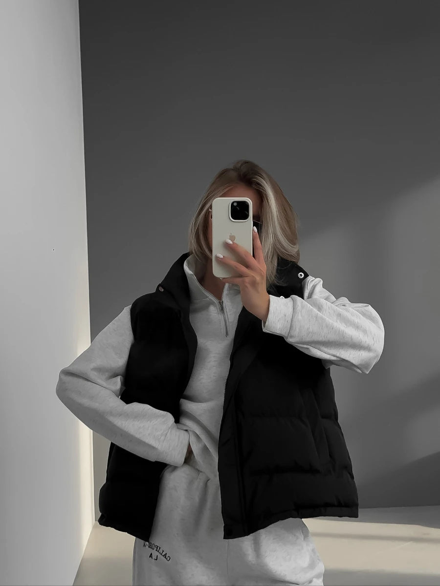 Colete acolchoado preto em xadrez sem mangas, usado sobre blusa cinza claro em selfie ao espelho